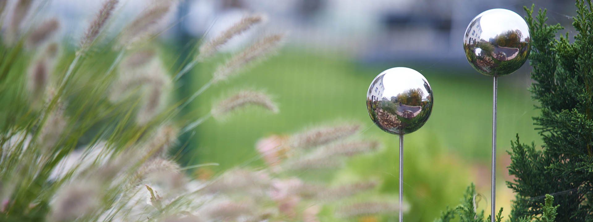 Gepflegte Gartenanlage mit Ziergr&auml;sern, Geh&ouml;lzen und dekorativen Gartenkugeln